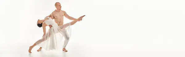 Un joven sin camisa y una mujer con un vestido blanco bailan con gracia, entrelazando y realizando movimientos acrobáticos en un entorno de estudio. - foto de stock