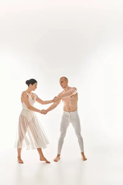 Un jeune homme torse nu et une jeune femme en robe blanche dansent ensemble, exécutant des éléments acrobatiques dans un décor de studio sur fond blanc. — Photo de stock