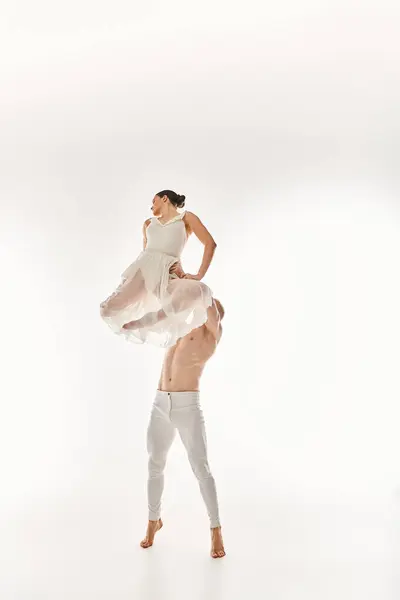 Un jeune homme torse nu et une femme en robe blanche dansent ensemble, exécutant des éléments acrobatiques dans un décor de studio sur fond blanc. — Photo de stock