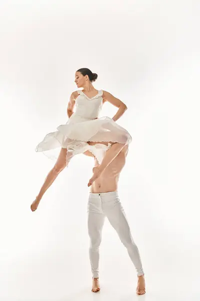 Мужчина без рубашки и женщина в белом платье танцуют вместе, исполняя акробатические элементы в студии на белом фоне. — стоковое фото