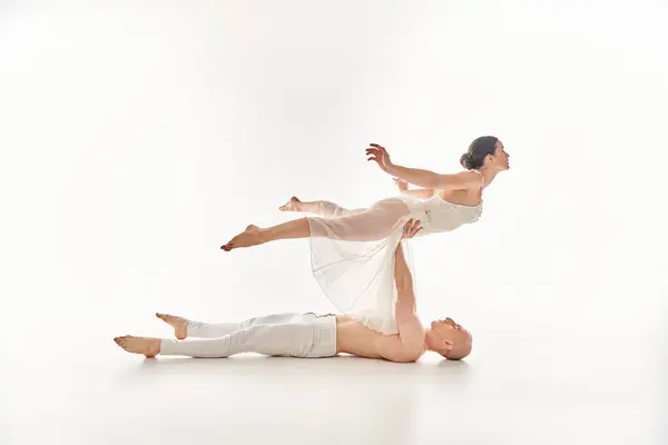 A shirtless young man and a woman in a white dress display grace and strength as they perform a split dance routine in a studio setting. — Stock Photo