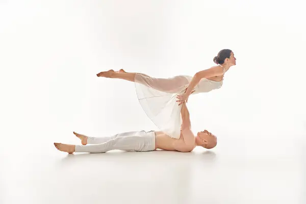 A shirtless young man and a woman in a white dress perform an elegant and acrobatic dance routine in a studio setting. — Stock Photo
