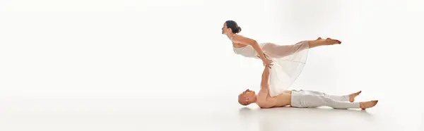 Young shirtless man and woman in white dress perform handstand together in studio setting. — Stock Photo