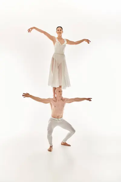 Без сорочки молодий чоловік і жінка в білій сукні витончено танцюють, демонструючи акробатичний баланс. — стокове фото
