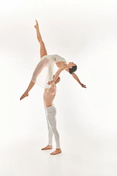Молодой человек без рубашки и женщина в белом платье изящно исполняют акробатические танцы в воздухе на белом фоне. — стоковое фото