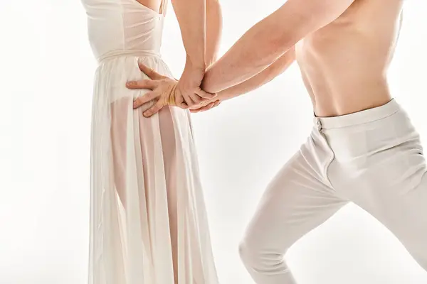 Un hombre joven, sin camisa y una mujer joven con un vestido blanco de pie entrelazado, tomados de la mano con gracia en una pose de baile. - foto de stock