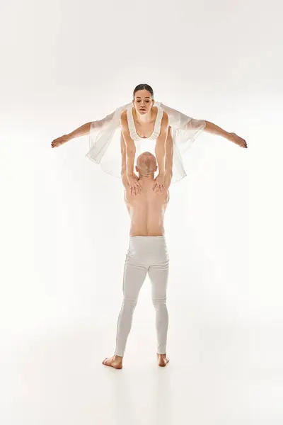 Um jovem sem camisa apoia uma mulher em um vestido branco enquanto se envolve em movimentos de dança acrobática. — Fotografia de Stock