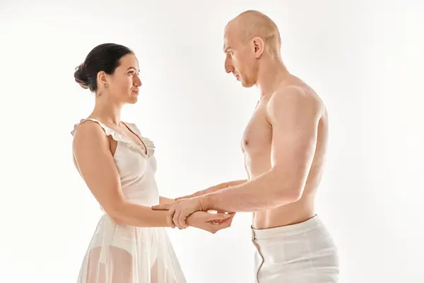 A shirtless young man and a woman in a white dress perform dance moves together in a studio against a white background. — Stock Photo
