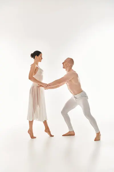 A shirtless man and a woman in a white dress perform acrobatic dance moves together in a studio setting. — Stock Photo