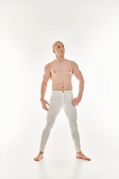 Молодий чоловік у білих штанях вражає динамічну позу, демонструючи акробатичні елементи на білому тлі. — стокове фото