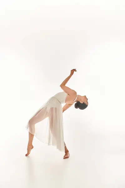A graceful young woman in a flowing white dress performs in a studio setting against a white background. — Stock Photo