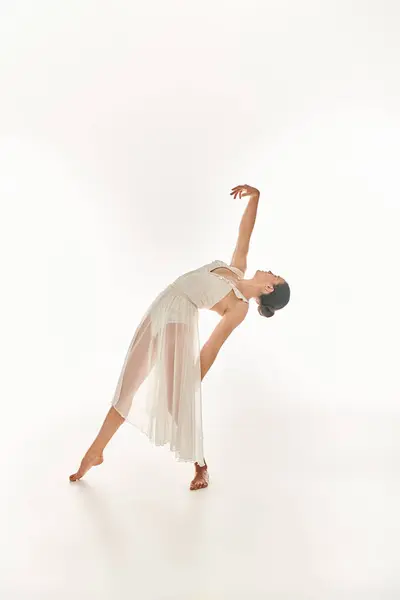 Graceful young woman in flowing white attire performs a perfect handstand in a studio setting against a clean white backdrop. — Stock Photo