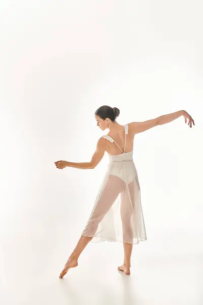 Jeune femme danse gracieusement dans une longue robe blanche, exsudant beauté et élégance dans un cadre de studio sur un fond blanc. — Photo de stock