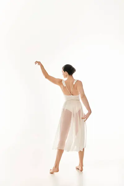Молода жінка зачаровує танцями у довгій білій сукні на білому тлі. — стокове фото