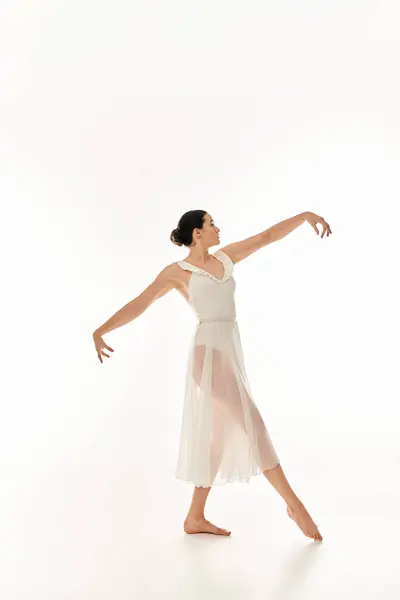 Une jeune femme respire la grâce en se déplaçant en robe blanche dans un décor de studio sur fond blanc. — Photo de stock