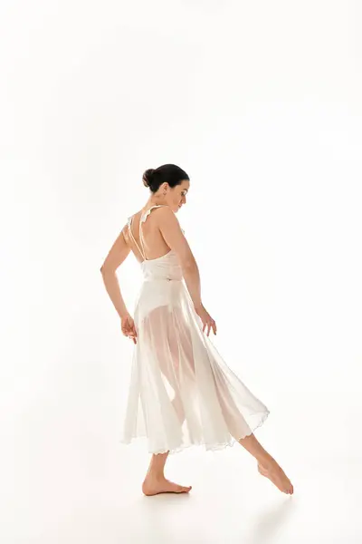 Молода жінка в білій сукні витончено танцює в студії на білому тлі. — стокове фото