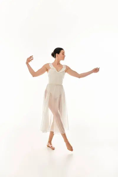 Une jeune femme danse gracieusement dans une longue robe blanche dans un décor de studio sur fond blanc. — Photo de stock