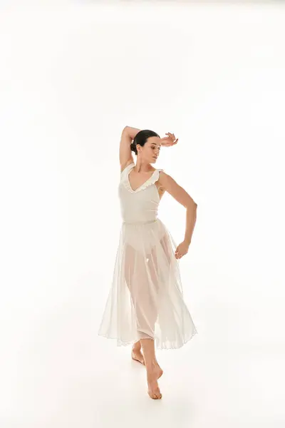 Une jeune femme gracieuse dans une robe blanche fluide oscille et virevolte dans un cadre de studio sur un fond blanc. — Photo de stock