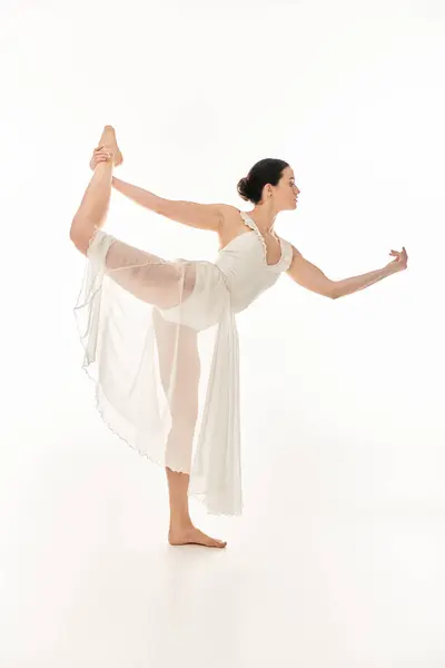 Une jeune femme dans une robe blanche fluide équilibre gracieusement sur un fond blanc propre. — Photo de stock