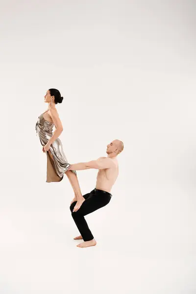 Un homme torse nu et une femme dans une robe brillante faisant élément acrobatique dans un cadre de studio. — Photo de stock