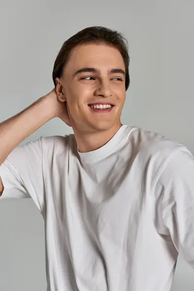 Fröhlich gut aussehender Mann in schlichtem T-Shirt posiert verführerisch vor grauem Hintergrund und schaut weg — Stockfoto