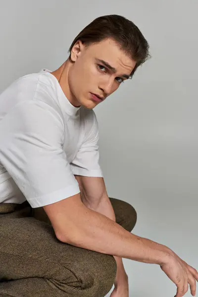Handsome polished young man in stylish clothing posing on gray background and looking at camera — Stock Photo