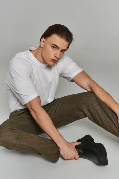 Appealing polished young man in stylish clothing sitting on gray background and looking at camera — Stock Photo