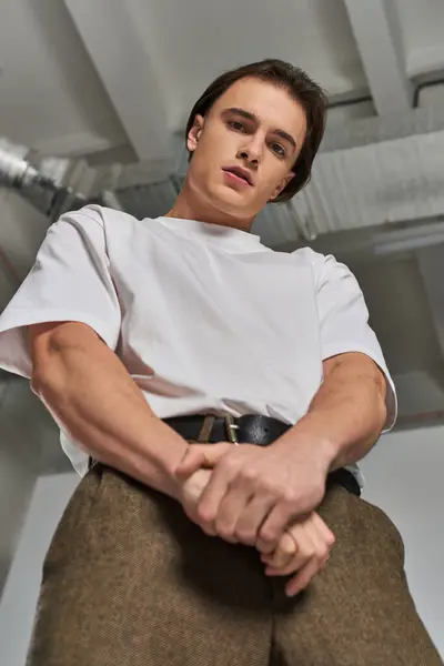 Modisches junges männliches Modell in eleganter Hose, das vor grauem Hintergrund in die Kamera blickt — Stockfoto