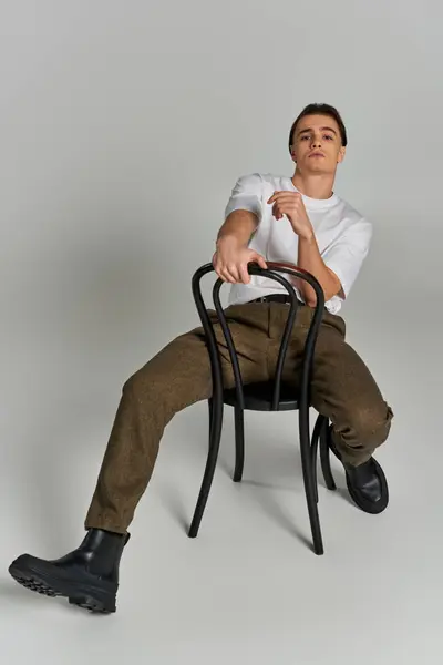 Bel homme élégant en tenue debonair assis sur la chaise et regardant la caméra sur fond gris — Photo de stock