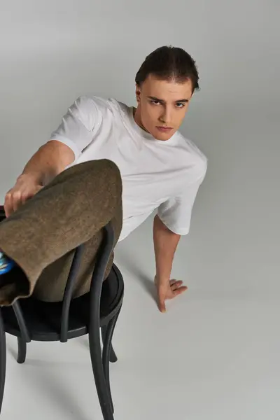 Handsome stylish man in debonair attire sitting on chair and looking at camera on gray backdrop — Stock Photo