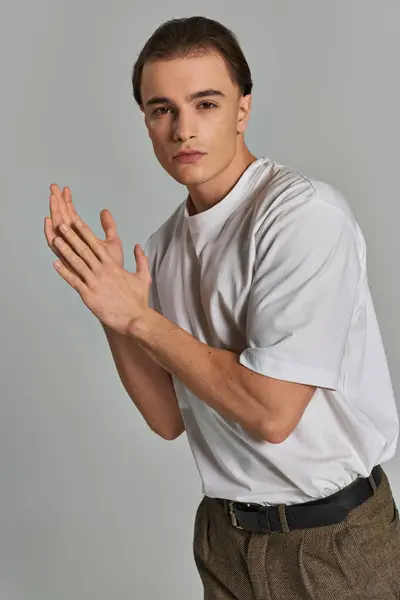 Modelo masculino jovem na moda em calças sofisticadas olhando para a câmera enquanto no fundo cinza — Fotografia de Stock