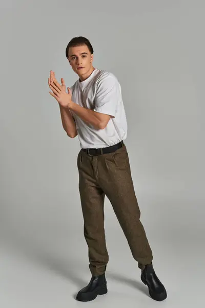Fashionable young male model in sophisticated pants looking at camera while on gray background — Stock Photo