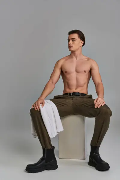 Sexy homme attrayant dans un pantalon brun sophistiqué posant seins nus tout en étant assis et regardant loin — Photo de stock