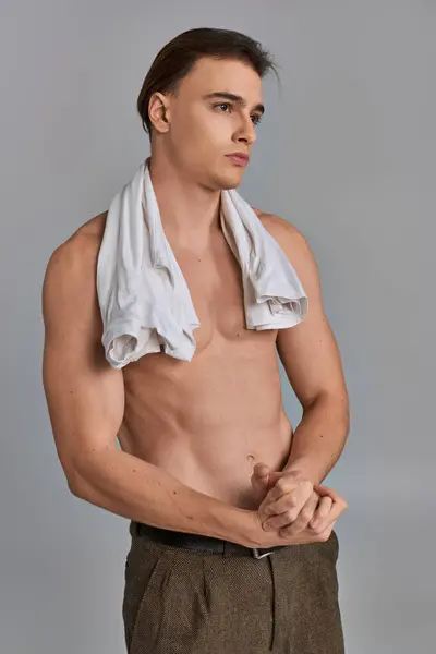 Séduisant beau jeune homme en pantalon brun posant seins nus sur fond gris et détournant les yeux — Photo de stock