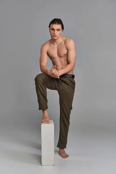 Enticing young shirtless male model in elegant pants posing alluringly and looking at camera — Stock Photo
