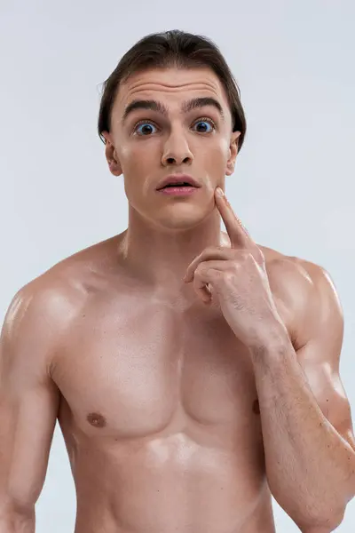 Shirtless handsome shocked man posing with finger near face and looking at camera on gray backdrop — Stock Photo
