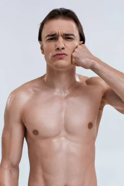 Guapo atractivo emocional modelo masculino posando en topless con el puño cerca de la mejilla y mirando a la cámara - foto de stock