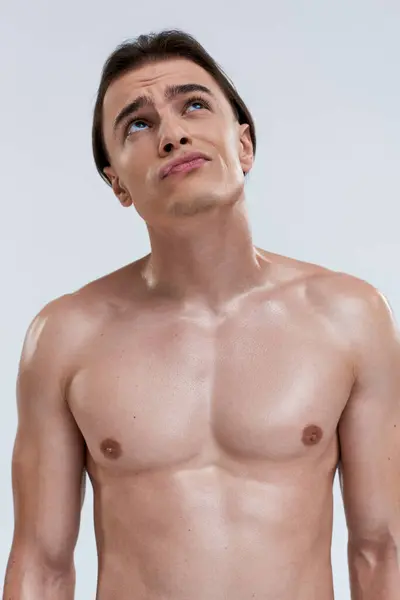 Concentrado buen aspecto joven modelo masculino posando en topless sobre fondo gris y mirando hacia otro lado - foto de stock