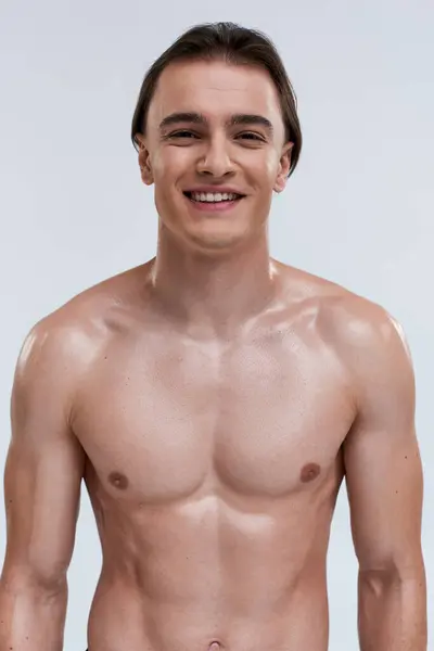 Cheerful alluring young male model posing topless and smiling happily at camera on gray backdrop — Stock Photo