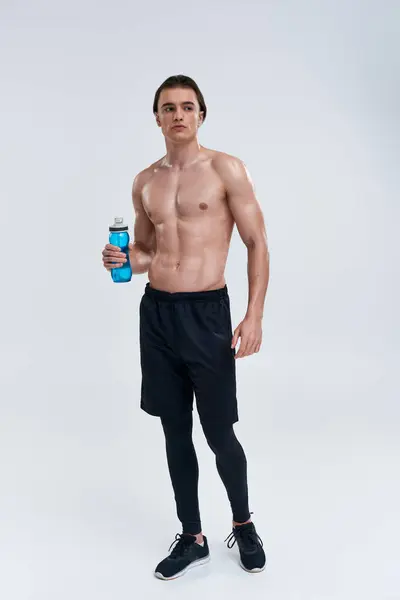 Handsome sexy male model in black pants holding water bottle and looking away on gray backdrop — Stock Photo