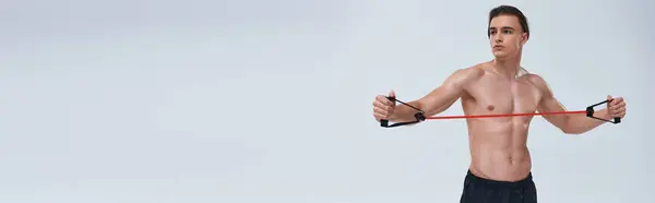 Tentador hombre deportivo sin camisa en pantalones negros de entrenamiento con expansor de fitness y mirando hacia otro lado, pancarta - foto de stock