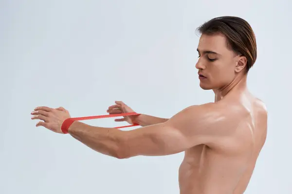 Alluring sporty young man in black pants posing topless with resistance band and looking away — Stock Photo