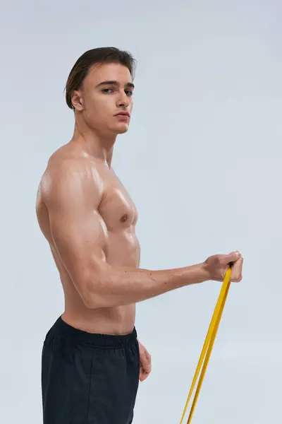 Sporty alluring young man posing topless while training with resistance band and looking at camera — Stock Photo