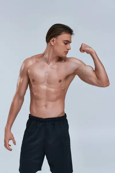 Sexy sin camisa atlético hombre en pantalones negros jugando sus músculos mientras posando sobre fondo gris - foto de stock