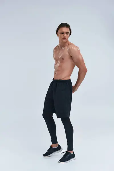 Athletic good looking young man posing shirtless in black pants and looking away on gray background — Stock Photo