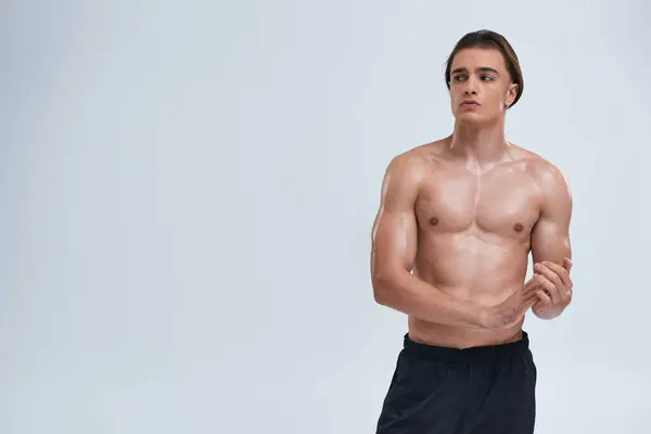 Athletic good looking young man posing shirtless in black pants and looking away on gray background — Stock Photo