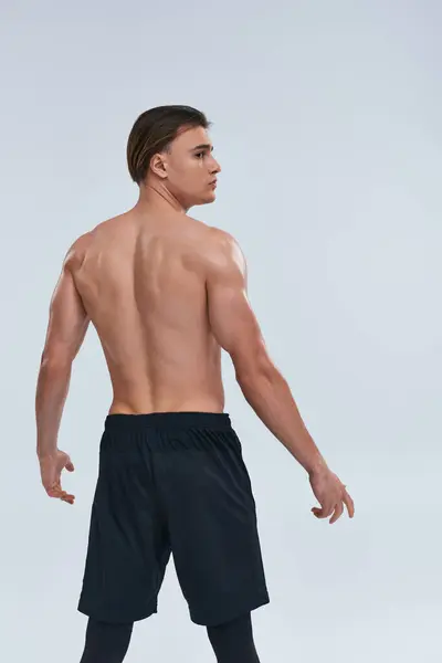 Athletic good looking young man posing shirtless in black pants and looking away on gray background — Stock Photo