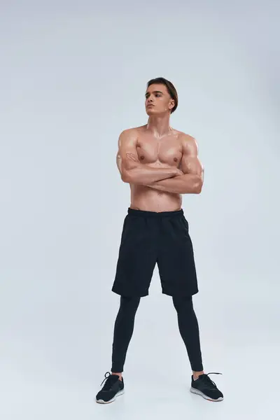 Good looking sexy shirtless man in black sporty pants posing on gray backdrop and looking away — Stock Photo