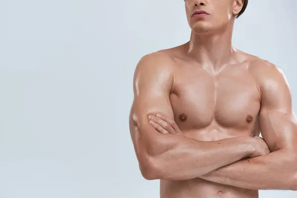 Cropped view of shirtless athletic man in black pants posing with crossed arms on gray backdrop — Stock Photo