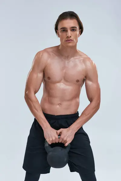 Handsome athletic shirtless man exercising with kettlebell and looking at camera on gray backdrop — Stock Photo